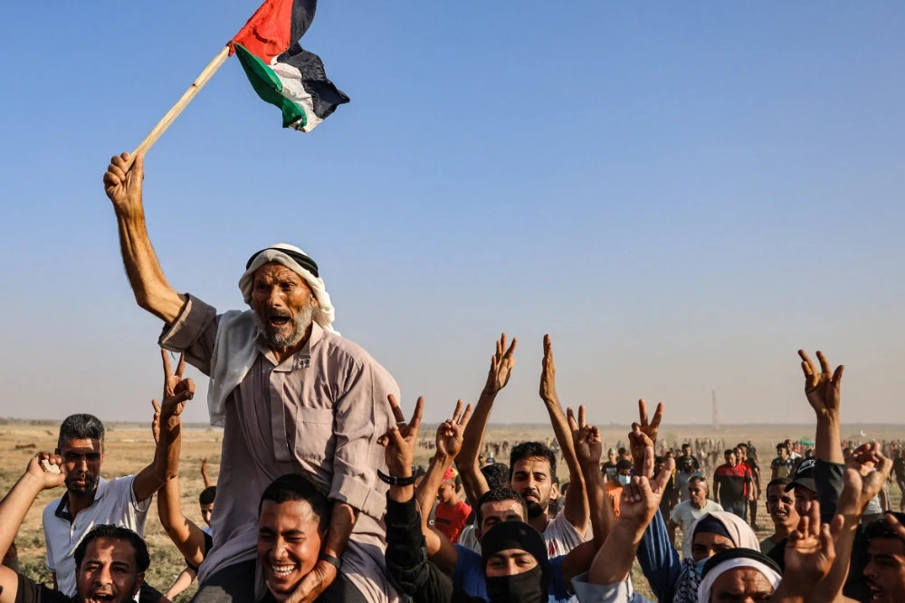 An elderly Palestinian man raises a national flag as youths shout slogans during a protest in the southern Gaza Strip. (AFP)