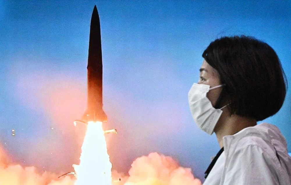 A woman walks past a screen showing a news broadcast with file footage of a North Korean missile test, at a railway station in Seoul on June 5, 2022. (AFP)