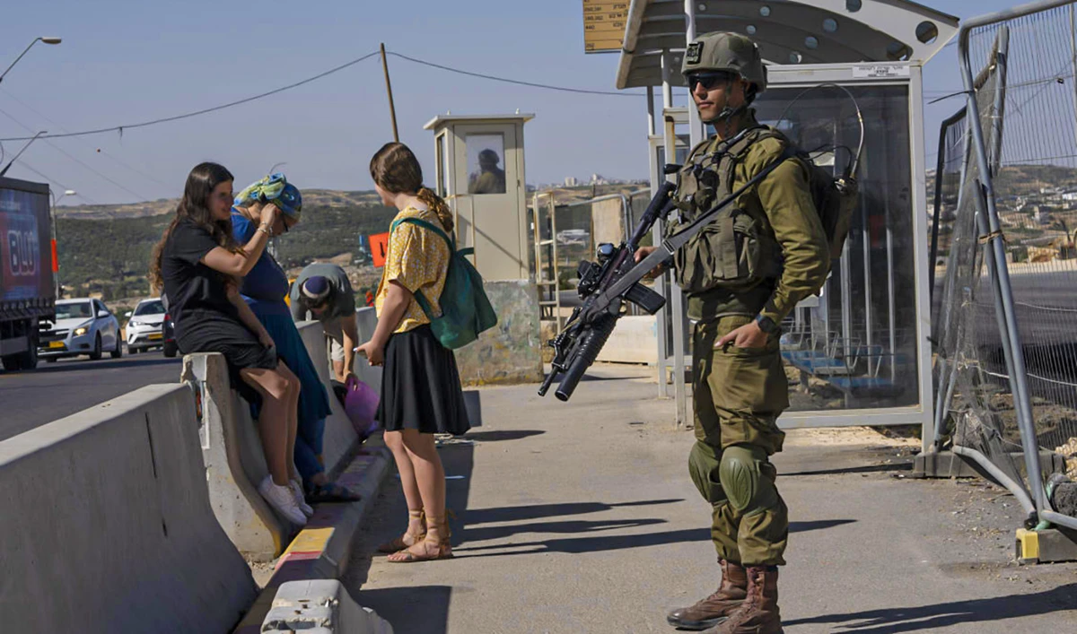 An Israeli soldier secures a bus stop while Israeli settlers wait for a ride at the Gush Etzion junction on June 9, 2022. (AP)
