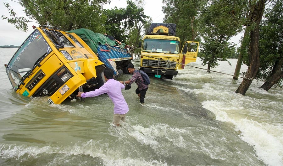 People wade past stranded trucks on a flooded street in Sunamganj on June 21, 2022. (AFP)