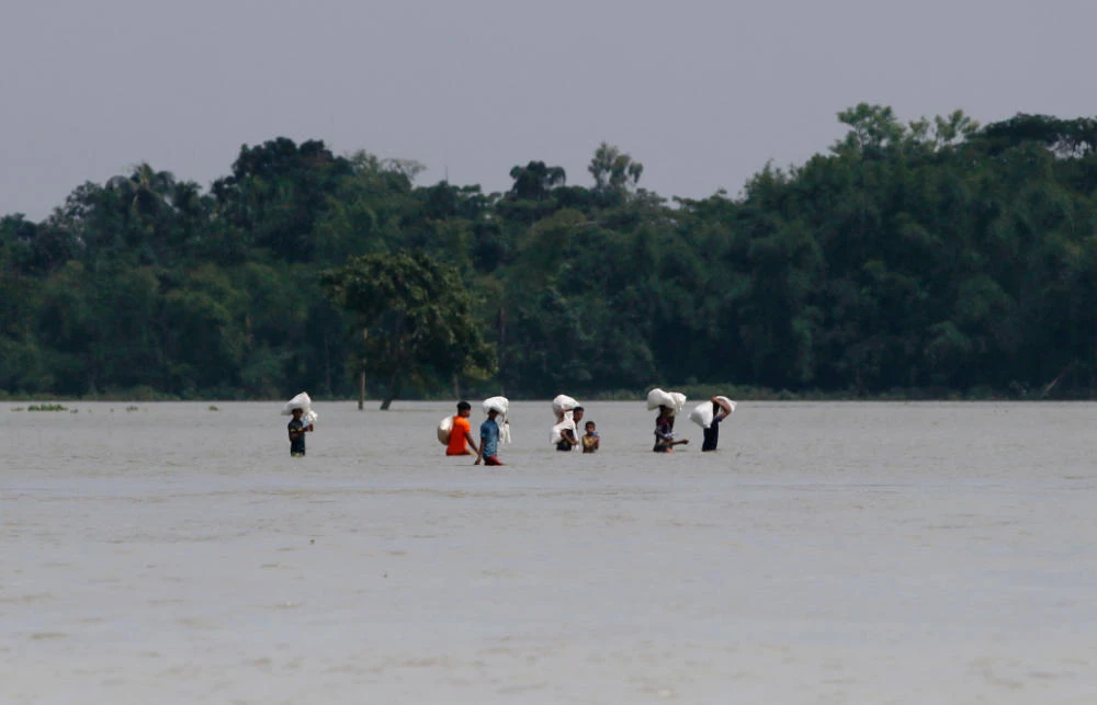 People wade along in a flooded area following heavy monsoon rainfalls in Companiganj on June 22, 2022, after collecting relief material. (AFP)