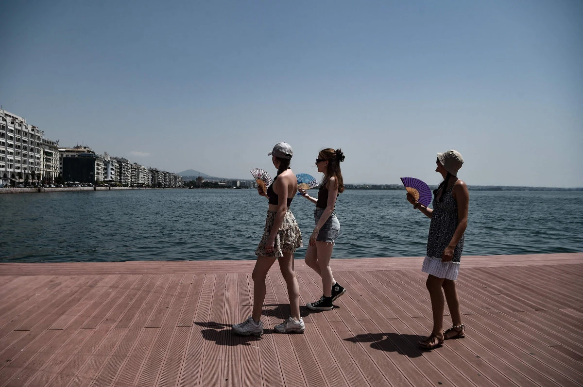 Pedestrians wave hand fans on the waterfront of Thessaloniki on June 23, 2022 amid a heatwave. (AFP)