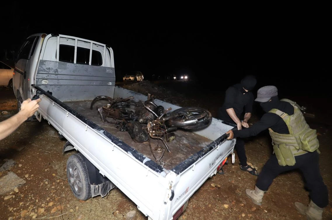 Militant fighters transport the remains of a motorcycle ridden by Abu Hamzah Al-Yemeni, who was targeted in a drone attack on the eastern edge of Syria’s rebel-held Idlib province early on June 28, 2022. (AFP)