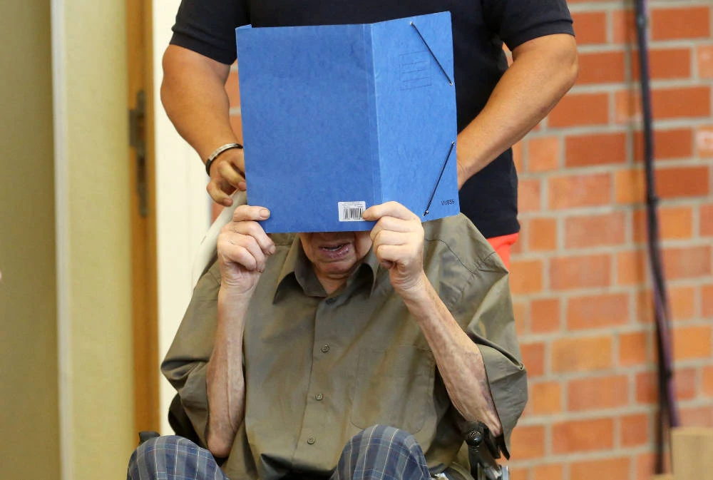 Former Nazi concentration camp guard Josef Schuetz hides his face behind a folder as he arrives on June 28, 2022 at a gym used as a makeshift courtroom in Brandenburg an der Havel, eastern Germany, where his verdict was spoken. (AFP)