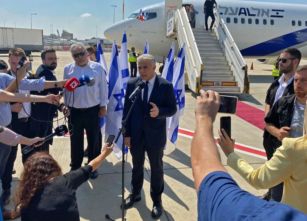 Israel’s Prime Minister Yair Lapid speaks to the press ahead of boarding his flight to France. (AFP)