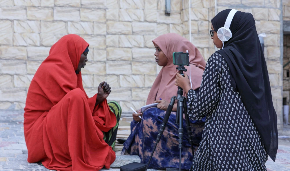 Two female journalists working for Bilan Media, a Somali start-up staffed entirely by women, interview a woman running a restaurant in a market in Mogadishu on May 22, 2022. (AFP)