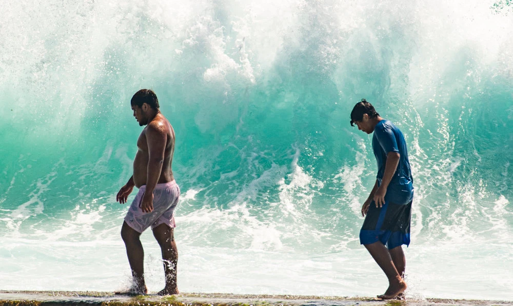 People walk in front of the high surf near Kapahulu Groin (Waikiki Wall) in Waikiki, Hawaii, Sunday, July 17, 2022. (AP)