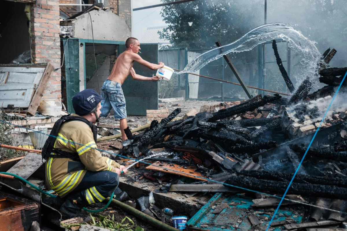 A local resident helps firefighters to put out a fire at a home in Bakhmut, Ukraine following a Russian airstrike on July 19, 2022 (Igor Tkachev / AFP)