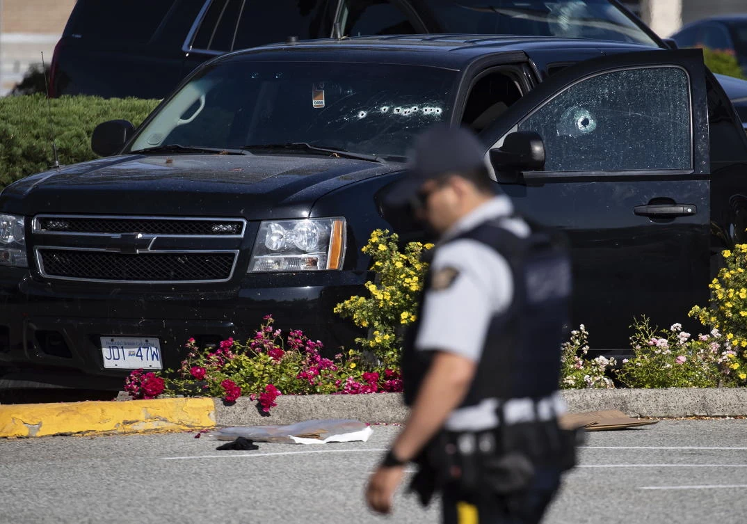 A police officer walks near a windshield and passenger window of a vehicle with bullet holes at the scene of a shooting in Langley, British Columbia on July 25, 2022. (The Canadian Press via AP)
