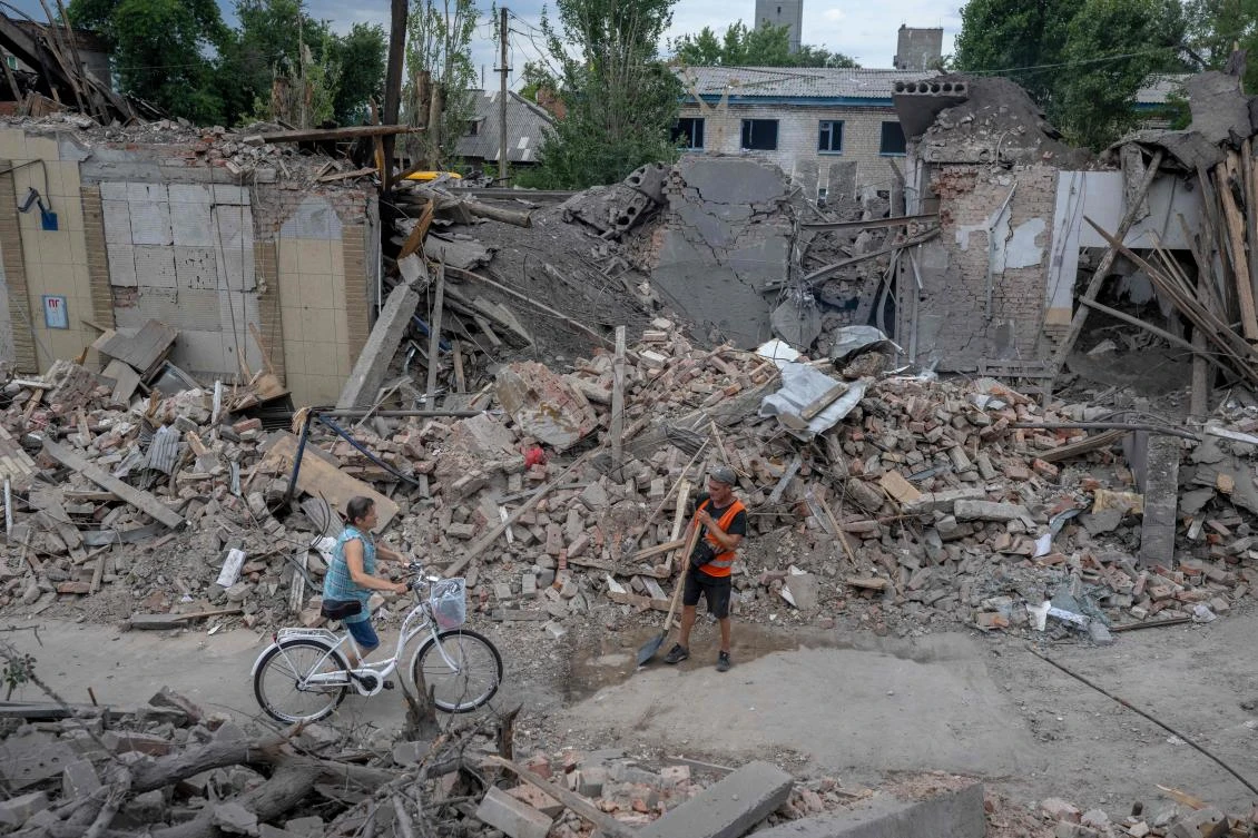 A local resident pushes her bicycle through damaged buildings in Toretsk, eastern Ukraine, on August 5, 2022, amid the Russian invasion of Ukraine. (AFP)