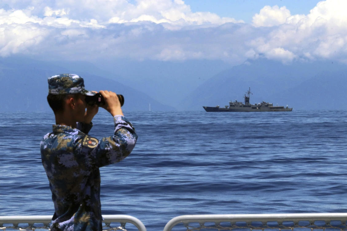 A People’s Liberation Army member looks through binoculars during military exercises as Taiwan’s frigate Lan Yang is seen at the rear on Aug. 5, 2022. (Xinhua via AP)