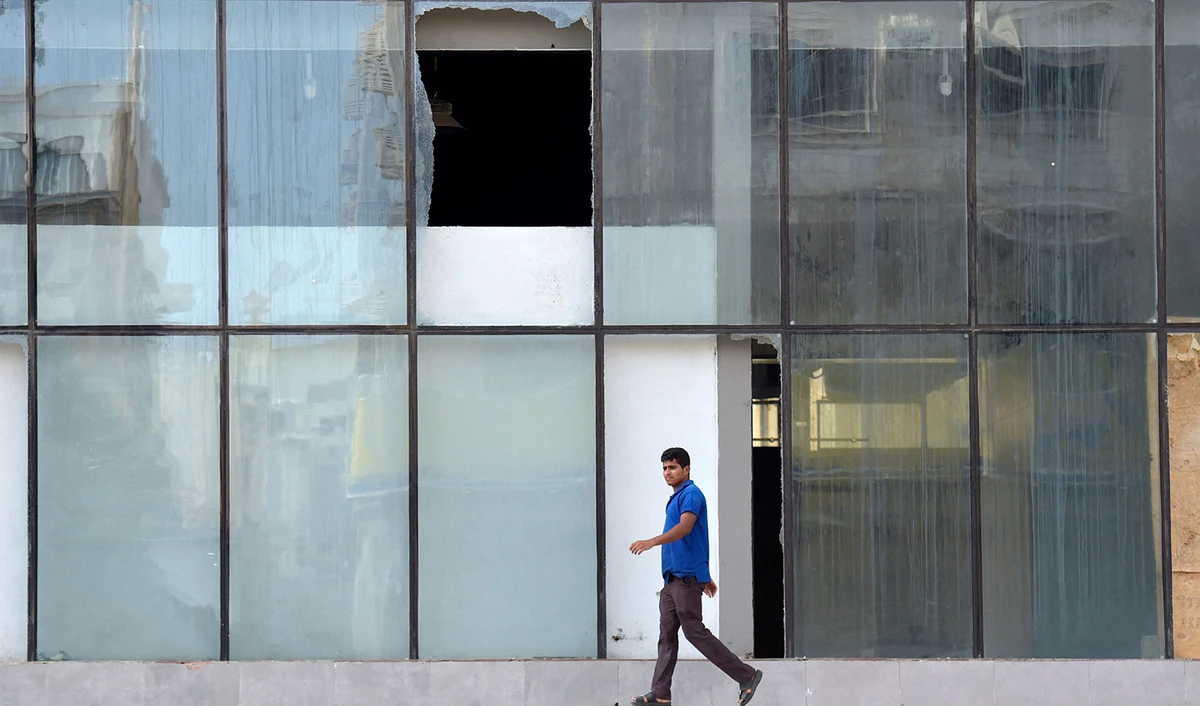 A picture taken on August 12, 2022 shows shattered glass as a man walks in front of the building where according to Saudi officials a wanted militant blew himself up while being arrested by security forces in Jeddah this week. (AFP)