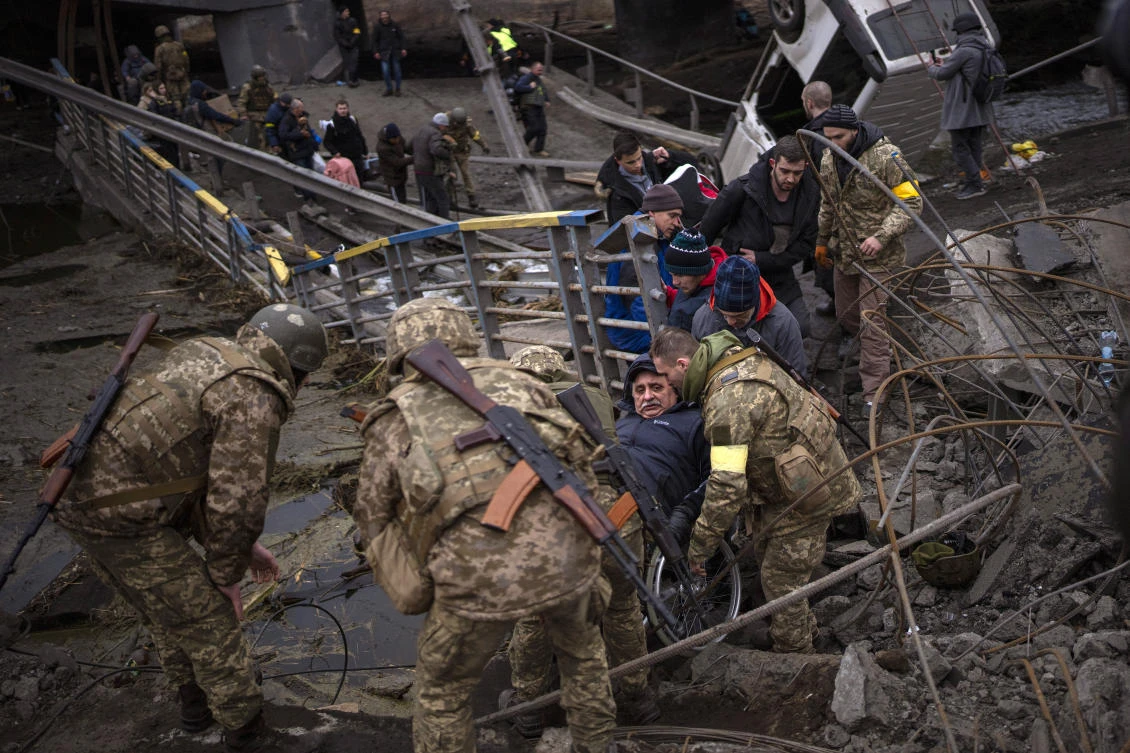 Ukrainian soldiers help a man in a wheelchair as people try to flee crossing the Irpin river in the outskirts of Kyiv, Ukraine. (File/AP)
