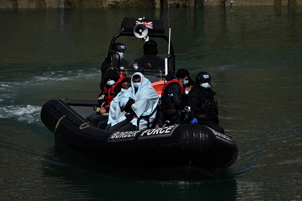 Above, UK border forces with migrants who were interdicted while attempting to cross the English Channel. (AFP file photo)