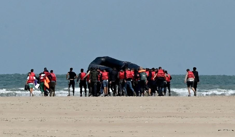Migrants push an inflatable boat across a stretch of sand toward the water, near Gravelines, northern France, on August 25, 2022, before they attempt to cross the English Channel to Britain. (AFP)