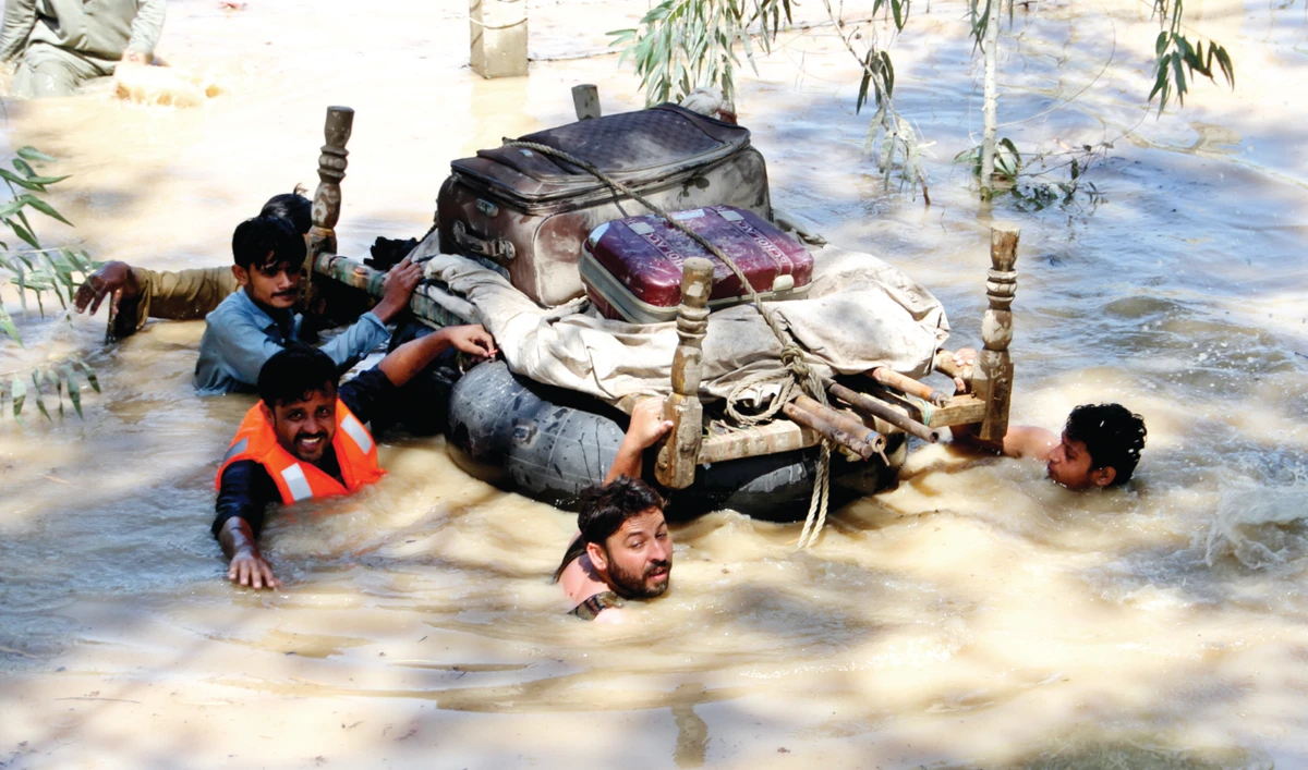 Displaced people float belongings salvaged from flood-hit homes through a flooded area on the outskirts of Peshawar on Sunday. (AP)