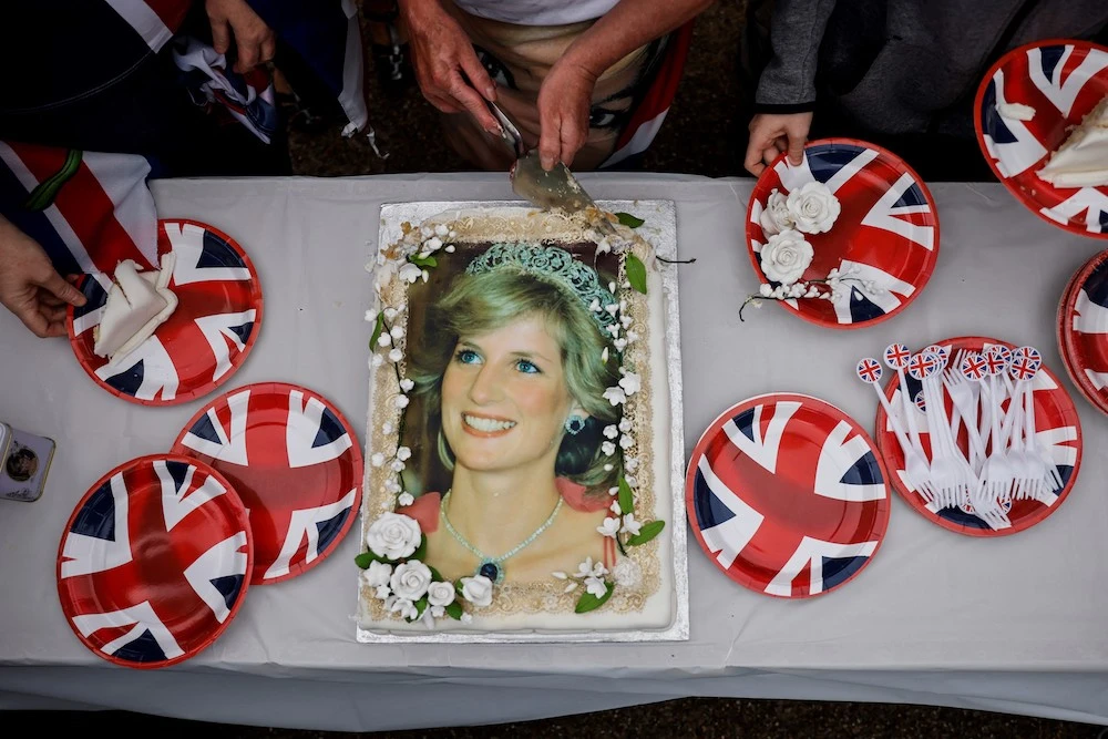 Visitors cut a cake depicting late Britain's Princess Diana in front of Kensington Palace, in central London, on August 31, 2022 during a gathering to pay a memorial tribute on the 25th anniversary of the Princess of Wales's death. (AFP)