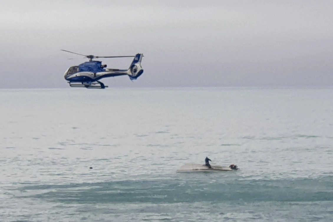 A rescue helicopter flies overs an upturned boat with a survivor sitting on the hull off the coast of Kaikoura, New Zealand on Sept. 10, 2022. (AP)