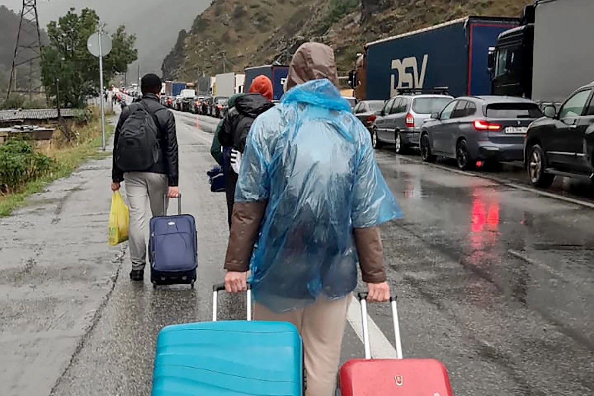 People carrying luggage walk past a long line of vehicles with Russian license plates at the customs checkpoint between Georgia and Russia on Sept. 25, 2022. (AFP)