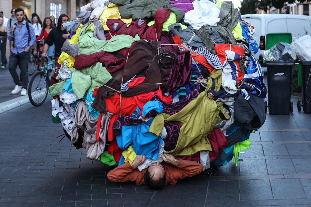 Actor and director Dorian Chavez (C) pushes a ball covered by clothes as part of a performance called "Sisypholia" denouncing the "absurdity" of overconsumption in Toulouse. (AFP)