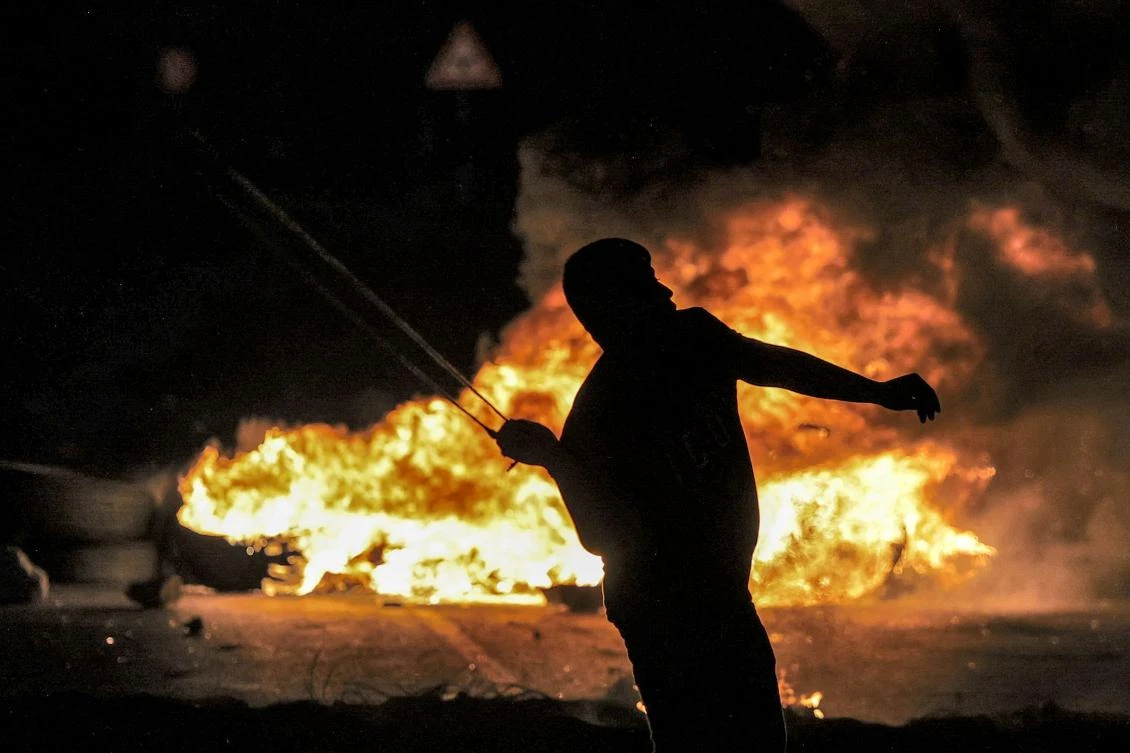 A Palestinian youth standing behind flaming tires throws a rock with a slingshot at Israeli security forces during clashes at the northern entrance of the city of Ramallah in the occupied West Bank on October 3, 2022. (AFP)