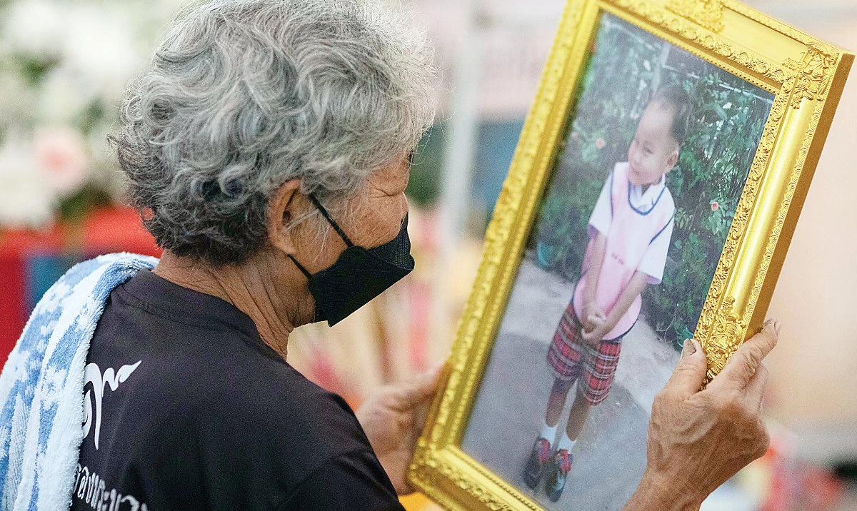 A grandmother looks at a photo of her grandchild, one of the victims of a mass shooting in the rural town of Uthai Sawan, northeastern Thailand. (AP)