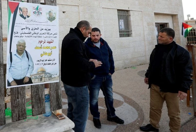 Men stand next to a poster of Palestinian-American Omar Abdalmajeed As’ad in Jiljilya village, Israeli-occupied West Bank, Jan. 12, 2022. (Reuters)