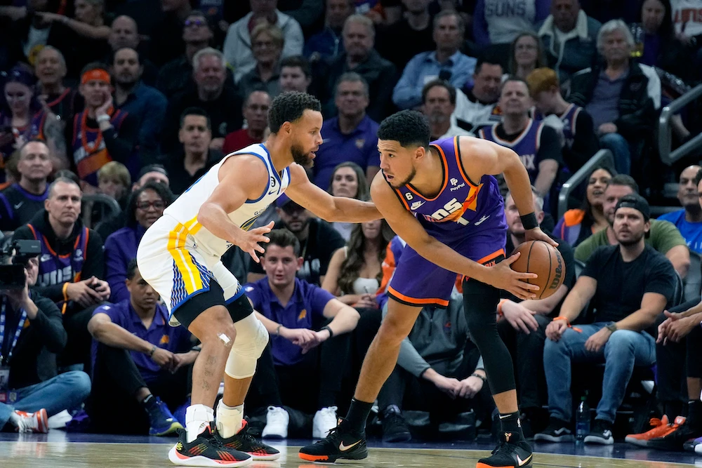 Golden State Warriors guard Stephen Curry and Phoenix Suns guard Devin Booker (1) face off during the first half of an NBA basketball game Tuesday in Phoenix. (AP)