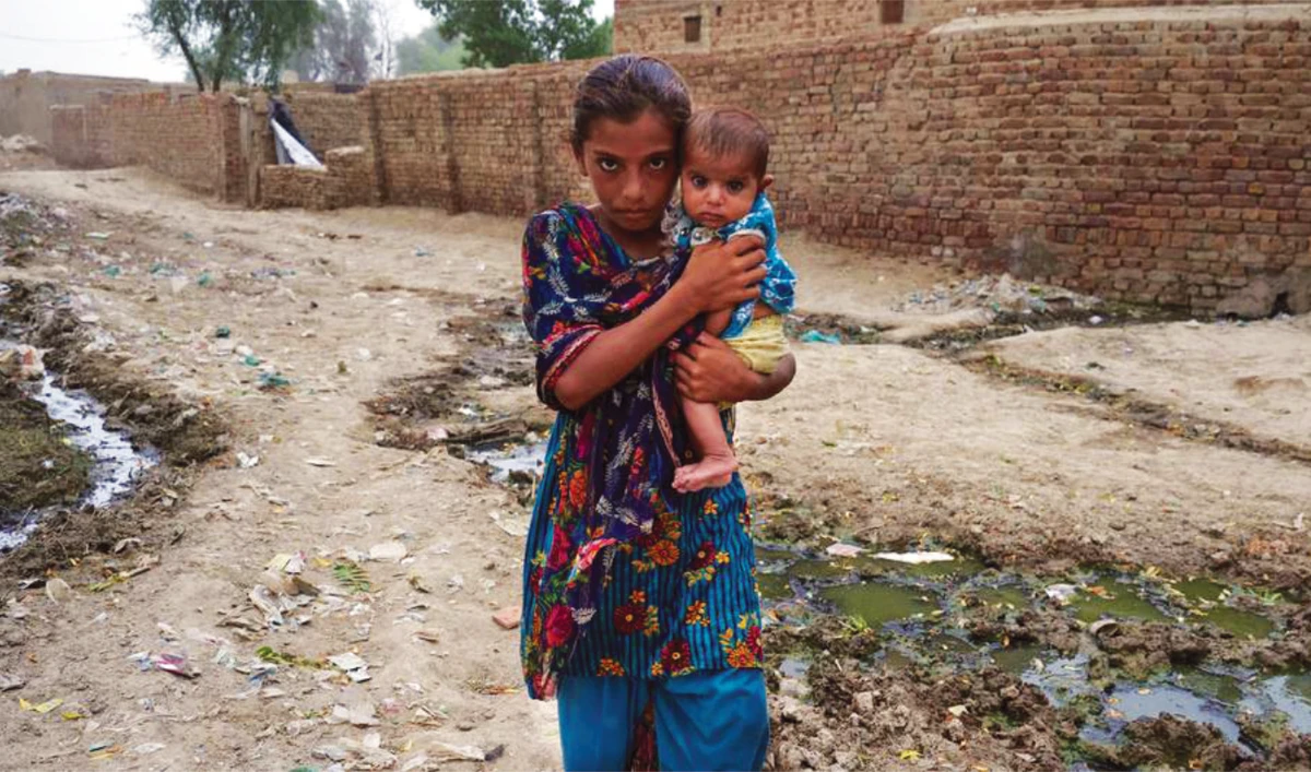 A girl holds a child as she makes her way to a mobile health clinic after their village was devastated by the floods in Pakistan. (UNICEF)