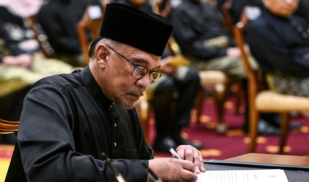 Malaysia's newly appointed Prime Minister Anwar Ibrahim signs documents after taking the oath during the swearing-in ceremony at the National Palace in Kuala Lumpur, Malaysia, on November 24, 2022. (Pool Photo via AP)