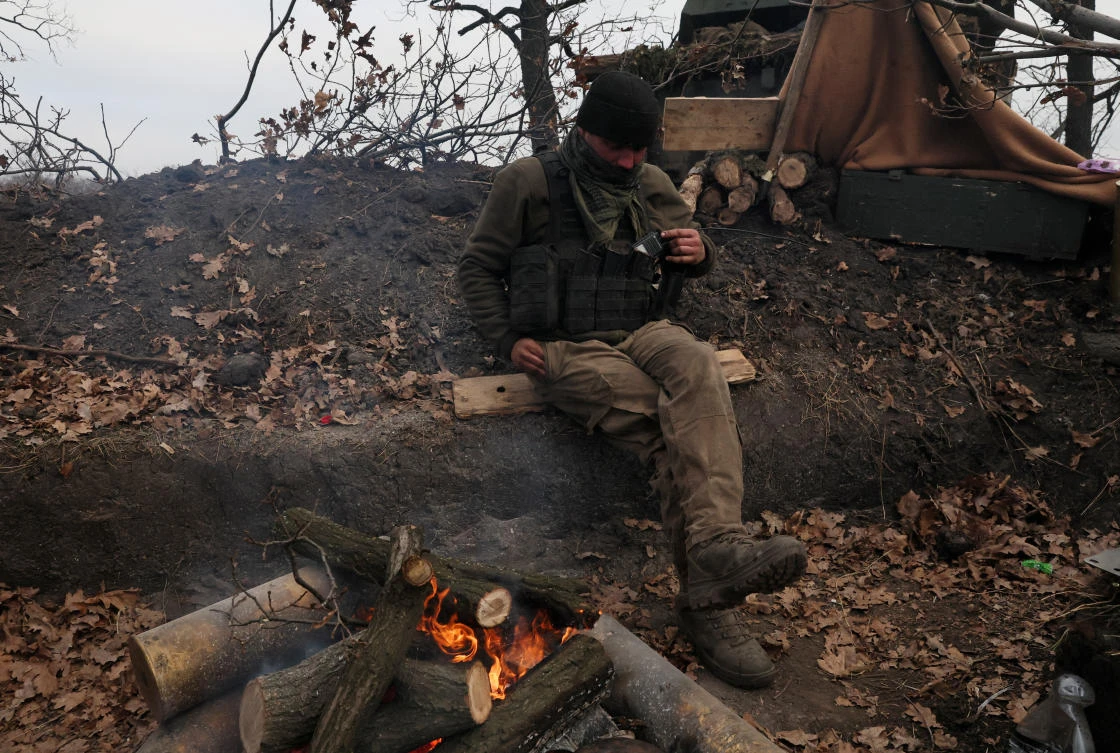 Above, an officer of the Ukrainian Army keeps warm by a fire to stave off the bitter cold while waiting for coordinates to strike a Russian military target. (Reuters)