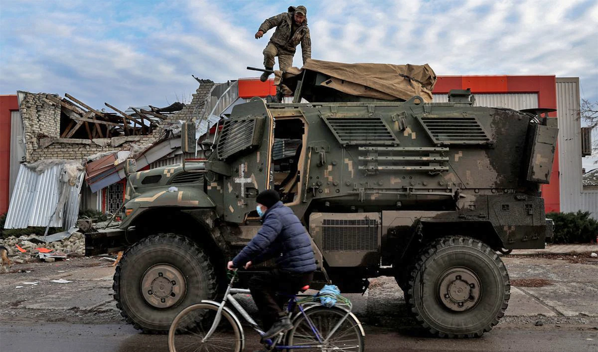 A man wearing a protective face mask rides a bike, as Russia's attack on Ukraine continues, past a soldier on an American MaxxPro military vehicle in the formerly Russian occupied city of Lyman, Donetsk region of Ukraine, on December 11, 2022. (REUTERS)