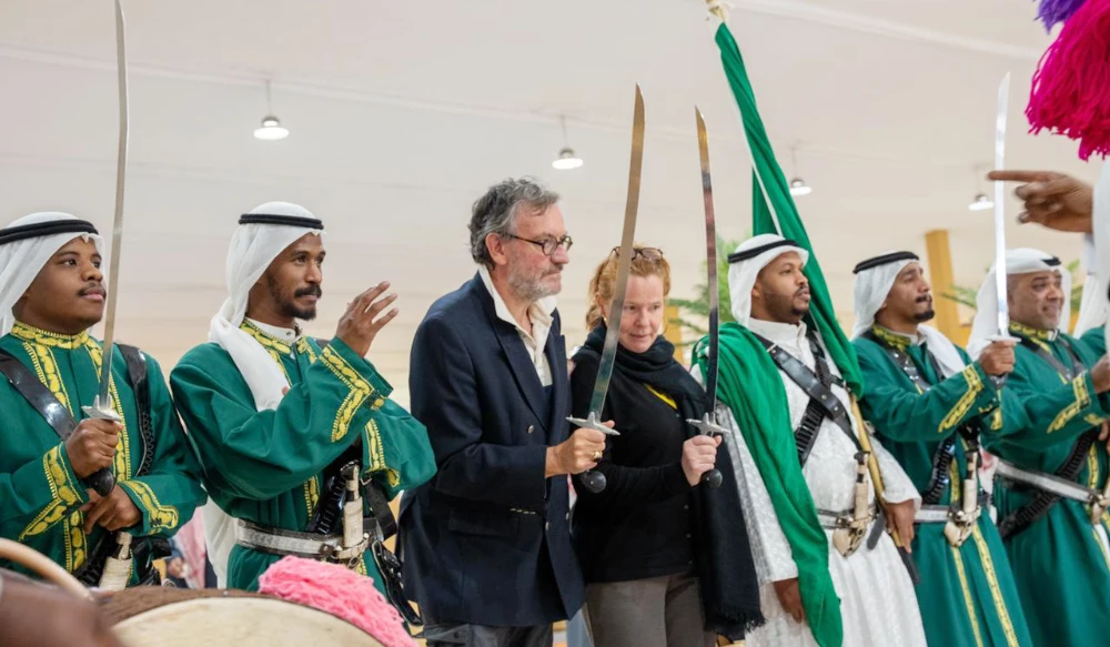 Pascal Grégoire, the Belgian Ambassador to the Saudi Arabia, with his wife, performed the ARDHA, a folkloric dance in Saudi Arabia. They are surrounded by men who performed the same dance with them, dressed in white clothes and covered with embroidered green robes. (Camel Club)