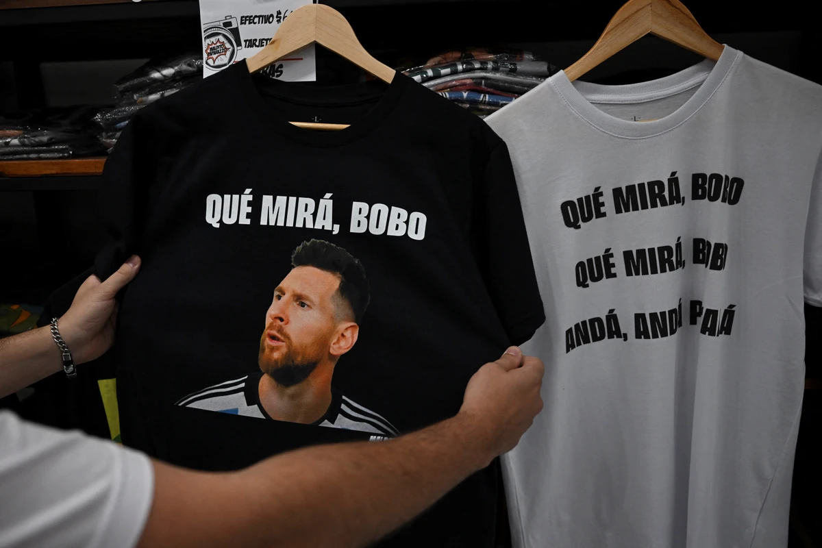 A man holds a t-shirt with an image of Argentine forward Lionel Messi and a phrase reading "What are you looking at, you fool?" at a store in Buenos Aires. AFP
