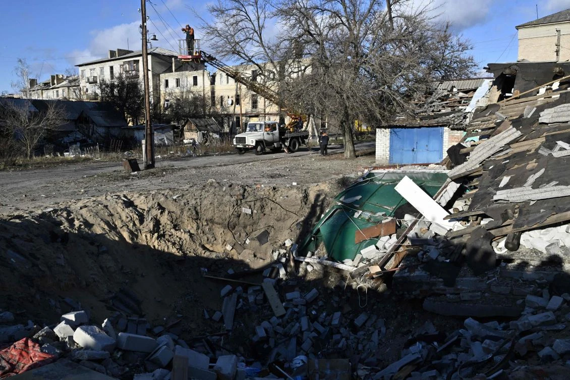 Workers repair power lines near a crater in the town of Lyman, Donetsk region, on December 14, 2022. (AFP)