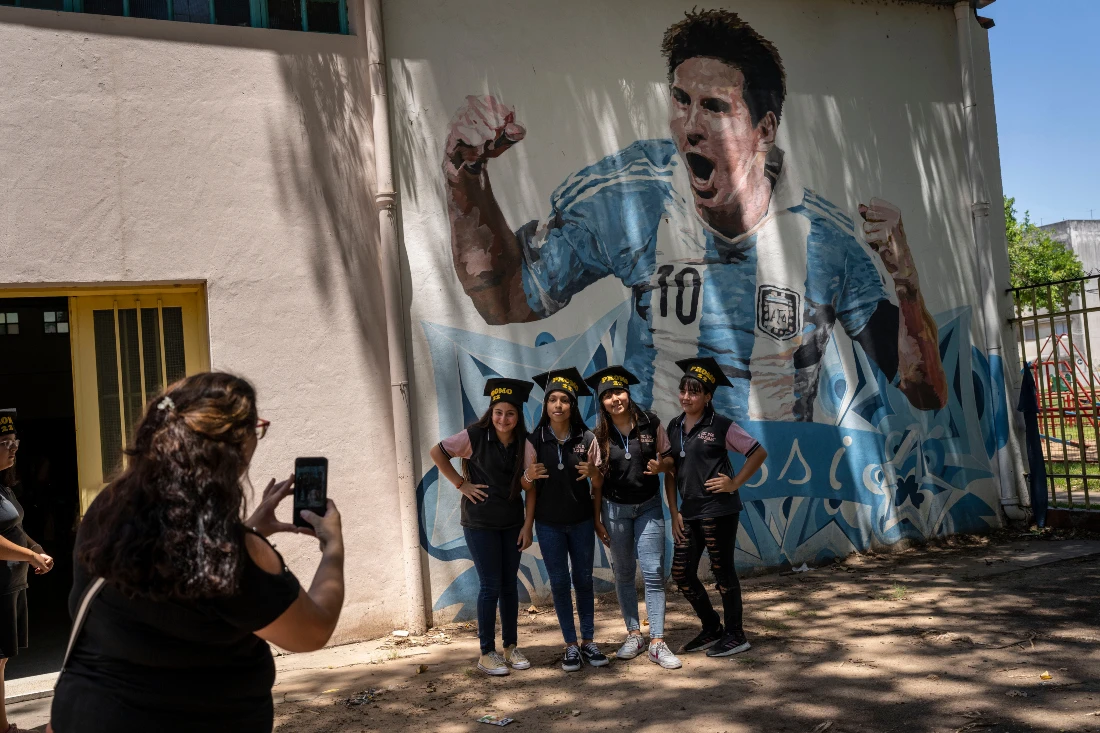 Students graduating from General Las Heras Elementary School, where Lionel Messi also studied, pose for group photo wearing their graduation hats by a mural of Messi. (AP)