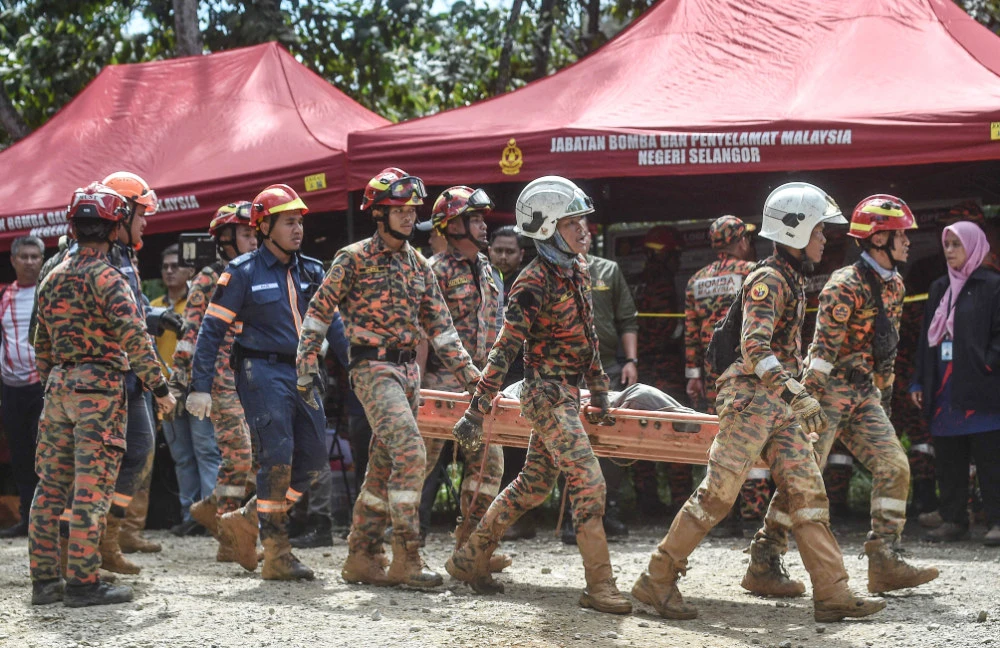 Fire and rescue department workers carry out the body of a victim after a landslide in Batang Kali, Selangor on December 16, 2022. (AFP)