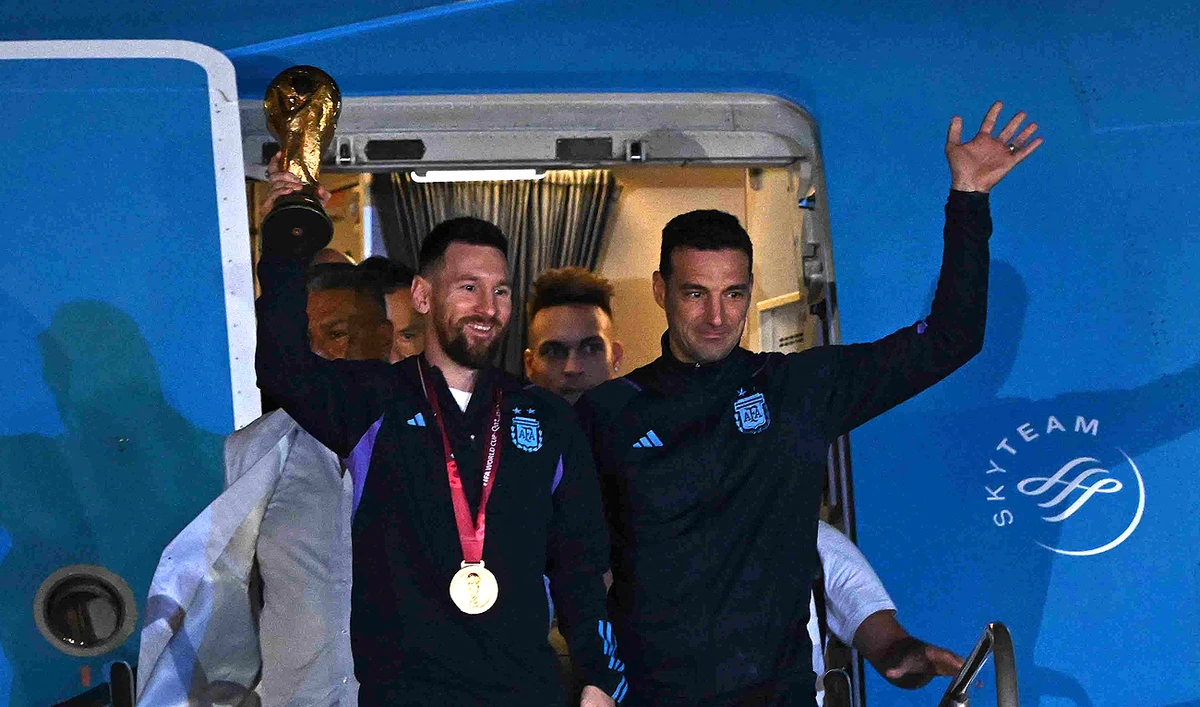 Argentina's captain and forward Lionel Messi (L) holds the FIFA World Cup Trophy alongside Argentina's coach Lionel Scaloni as they step off a plane upon arrival at Ezeiza International Airport after winning the Qatar 2022 World Cup tournament in Ezeiza, Buenos Aires province, Argentina on December 20, 2022. (Photo courtesy: AFP)