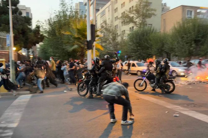 An Iranian police officer, center, raises a baton to disperse demonstrators during a protest in Tehran. (AFP)