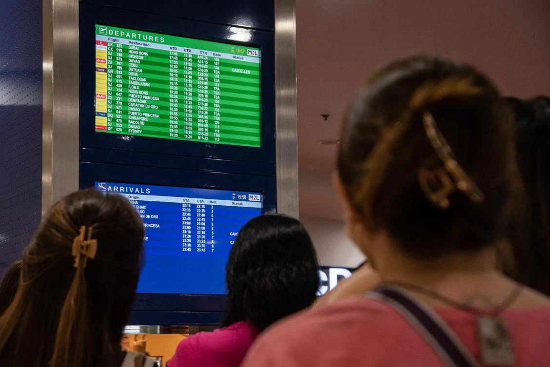 Passengers look at a screen showing flight information at terminal 3 of Ninoy International Airport in Pasay, Metro Manila on January 1, 2023. (AFP)