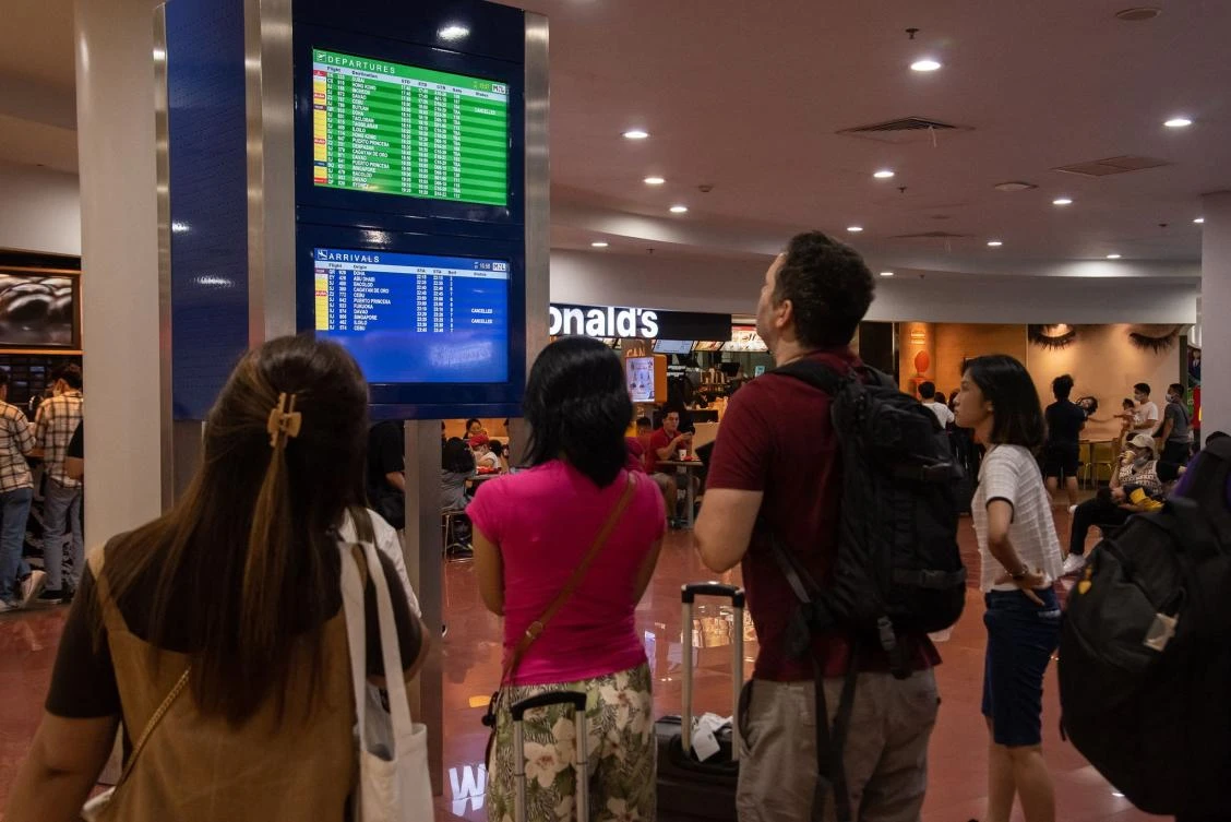 Passengers look at a screen showing flight information at terminal 3 of Ninoy International Airport. (AFP)