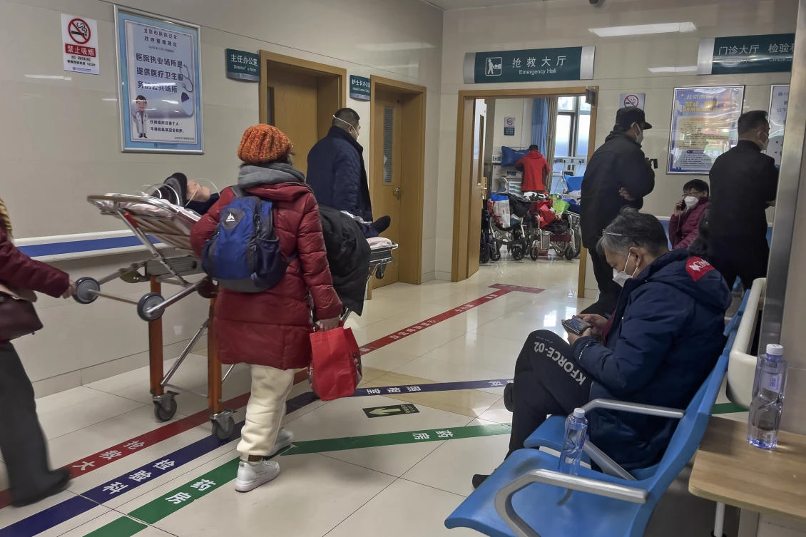 A man, right, browses his smartphone on a bench as an elderly patient is wheeled to an emergency hall in a hospital in Beijing, Saturday, Jan. 7, 2023. (AP)