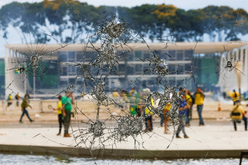 Supporters of Brazil's former President Jair Bolsonaro are pictured through a broken glass as they demonstrate against President Luiz Inacio Lula da Silva, outside Brazil’s National Congress in Brasilia, Brazil, January 8, 2023. (REUTERS)
