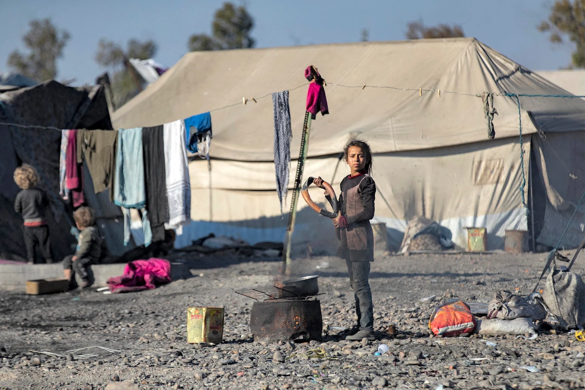 A girl holds an old steering wheel cover while standing by a cooking fire at a camp near Syria's northern city of Raqa. (File/AFP)
