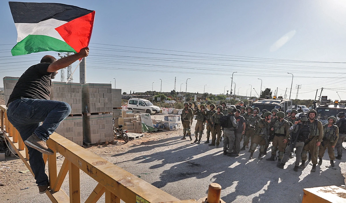 A Palestinian man carrying a national flag tries to jump a barrier guarded by Israeli security forces, during a demonstration by Palestinians and Israeli peace activists against settlement expansion, in the occupied West Bank town of Salfit, on July 27, 2022. (AFP)