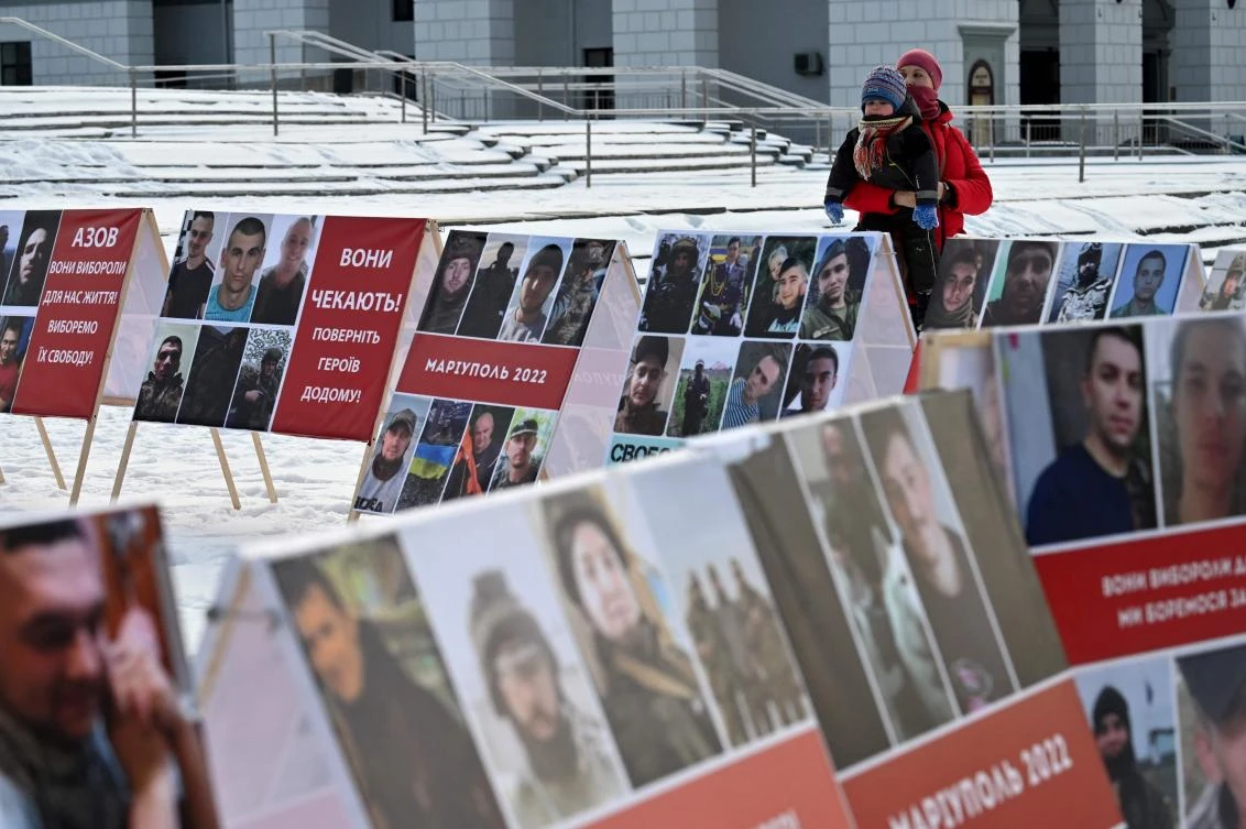 A relative of Ukrainian servicemen said to be captured by Russian forces, holds a child as she stands next to their portraits during their rally at Independence Square in Kyiv, as they call to hasten their release from Russian captivity according to the formula "All for All". (AFP)