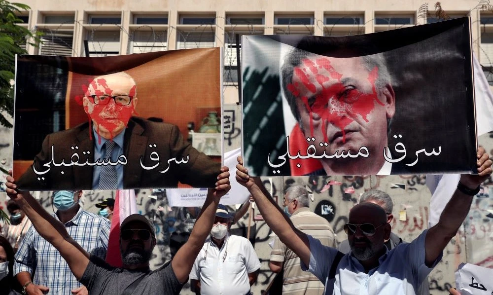 Bank customers hold up posters of Central Bank Governor Riad Salameh, right, and Secretary General of the Association of Banks in Lebanon Makram Sadir, Beirut, Lebanon, Oct. 6, 2021. (AP Photo)