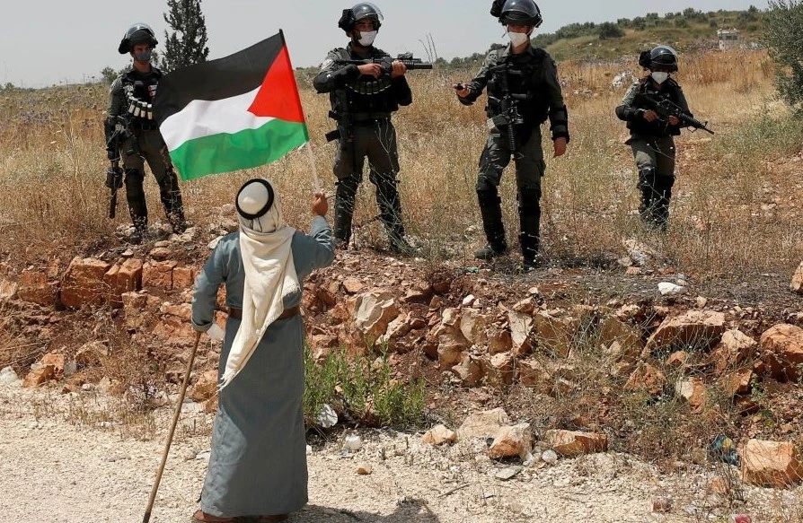 A demonstrator holds a Palestinian flag in front of Israeli forces, near Tulkarm, occupied West Bank, June 5, 2020. (Reuters)
