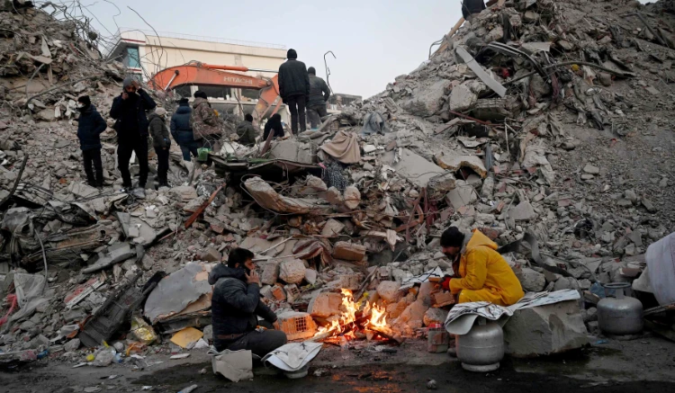 Relatives warm up around a fire in front of rubble of collapsed buildings in Kahramanmaras. (AFP)