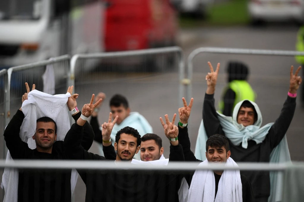 Detainees inside the Manston short-term holding centre for migrants, wave to members of the media outside, near Ramsgate, south east England on November 3, 2022. (AFP)